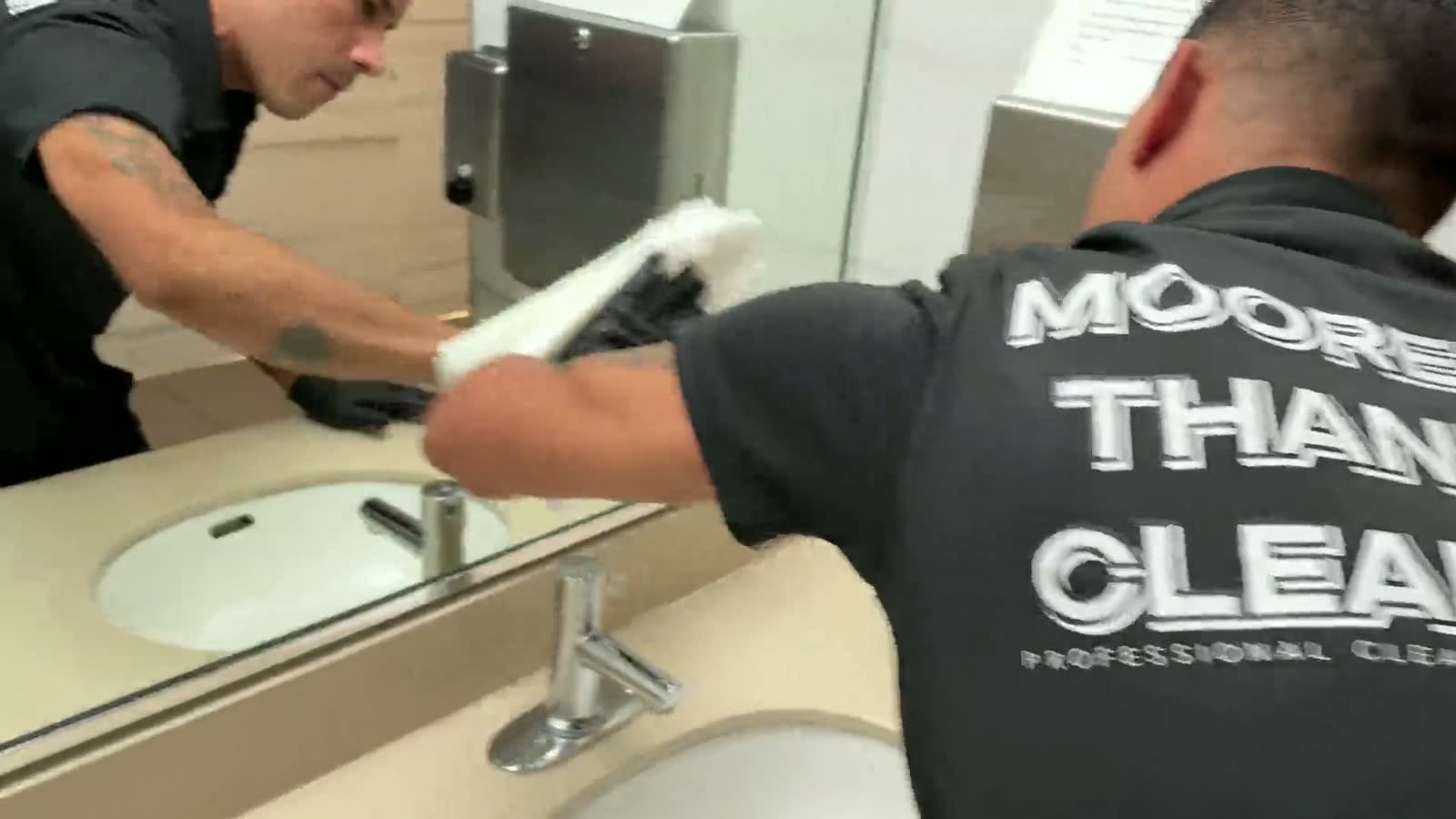 A cleaner disinfecting a restroom sink and counter
